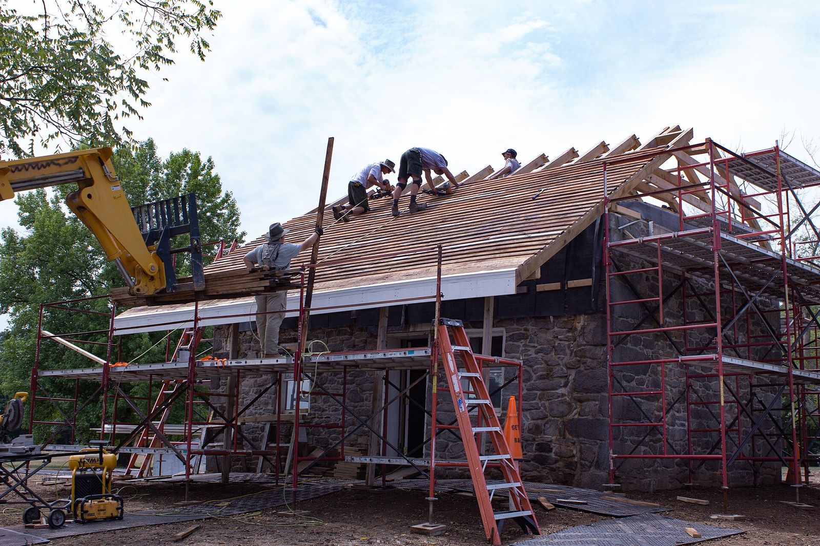 Three Rivers crew installing decking near the ridge of a steep roof with a telehandler lifting material